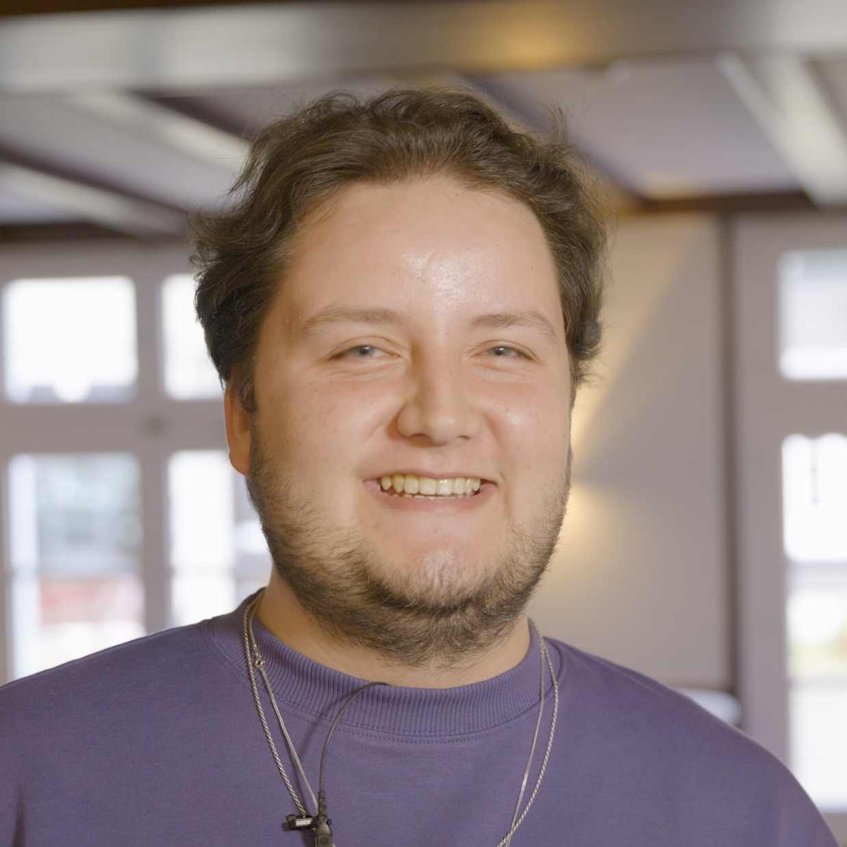 Porträts eines jungen Mannes in lila Pullover lächelt in die Kamera.